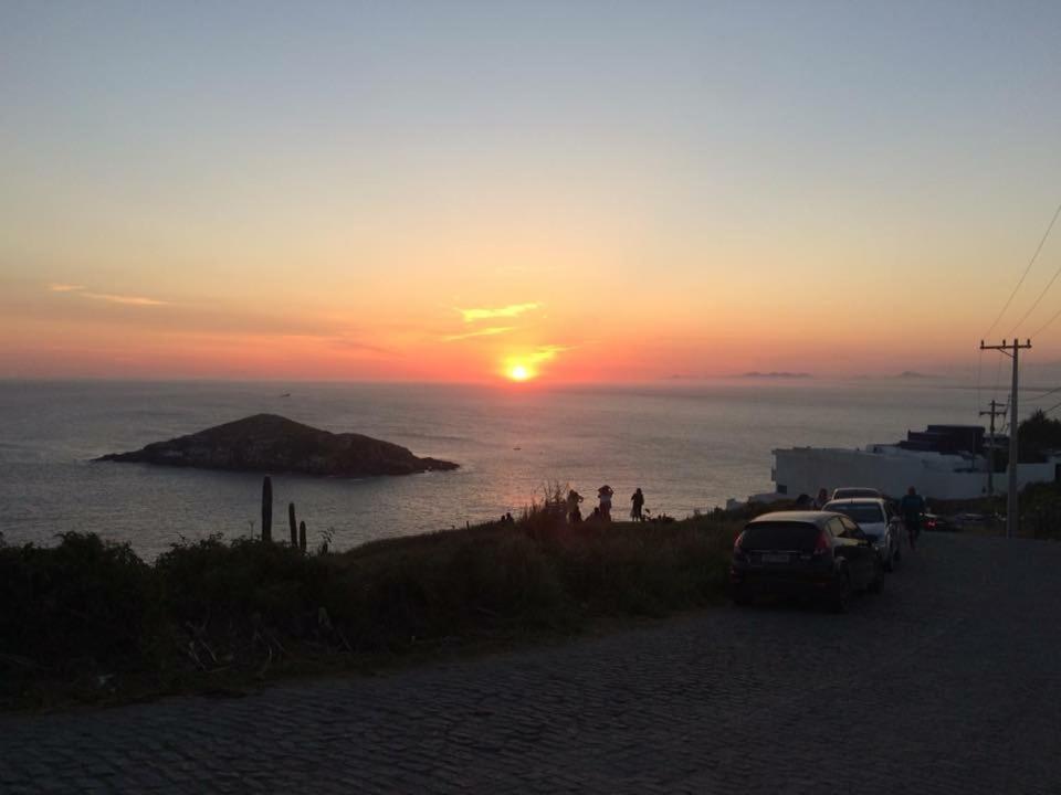 una puesta de sol sobre el océano con coches estacionados en una playa en Suítes dos anjos!, en Arraial do Cabo