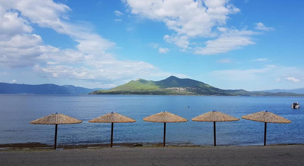 a row of straw umbrellas on a beach near the water at Mamanis Studios in Loutra Edipsou