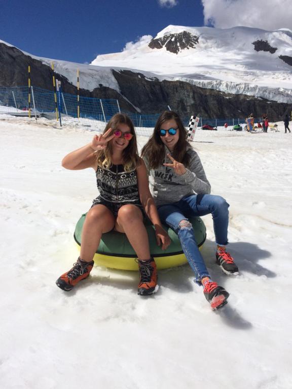 two girls sitting on a snow board in the snow at B&B Haus Granit Saas Grund in Saas-Grund