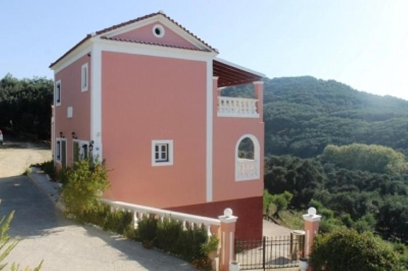 een groot rood huis met een balkon op een heuvel bij Villa Leonidas in Agios Stefanos