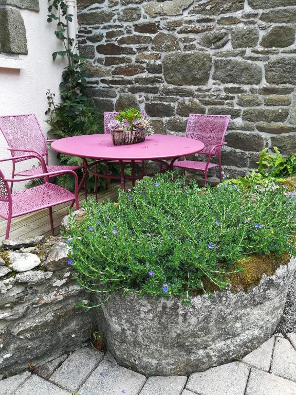 a pink table and chairs and a stone wall at Chez Herveline Le Fer - Chambres et table d'hôtes in Plouigneau