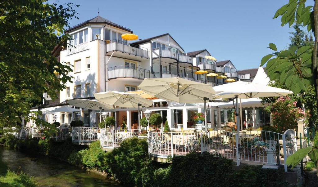 a building with tables and umbrellas next to a river at ANGERHOF Kur- und Thermenhotel in Bad Wörishofen