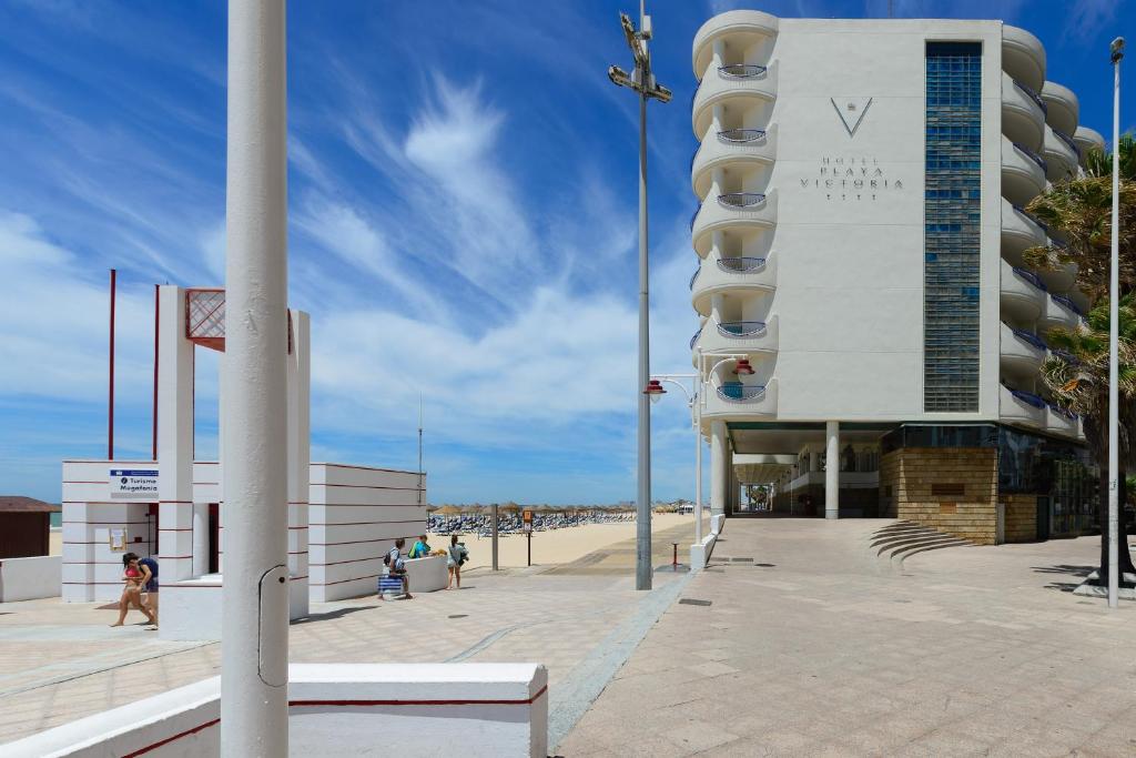a building on the beach with people walking on the beach at Hotel Playa Victoria in Cádiz