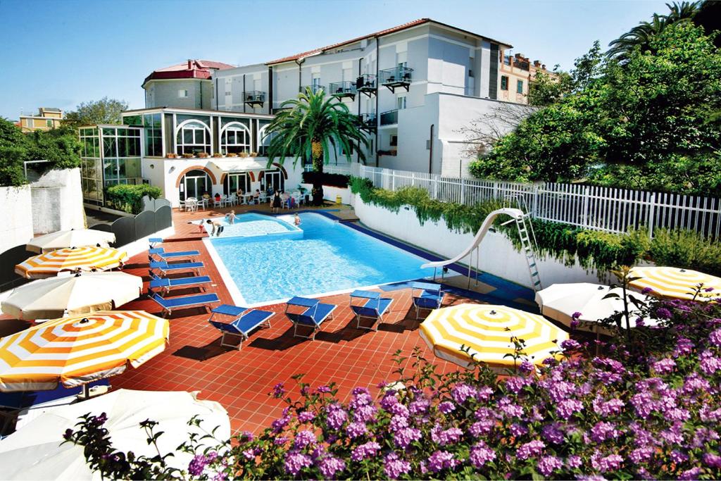 una piscina con sombrillas y sillas junto a un edificio en Hotel Riviera 3 Stelle con piscina estiva e campo tennis gratuiti e garage a pagamento, en Spotorno
