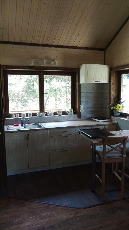 Bright kitchenette with large windows, sink, countertop, bar stool, mugs on windowsill.
