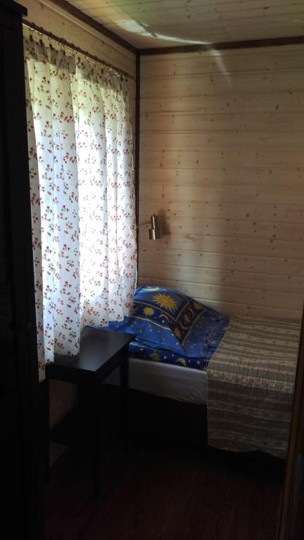 Compact single bed beside floral-curtained window, colorful sun-themed pillow and small bedside table.