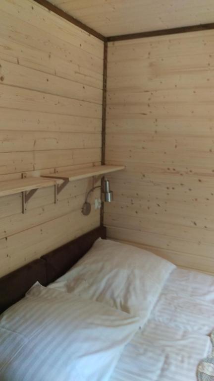 Pillow and neatly made bed beneath wall shelf and adjustable reading lamp in wooden room.