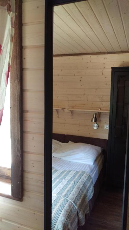 Narrow bedroom reflected in mirror, single bed with striped quilt against light wooden walls.