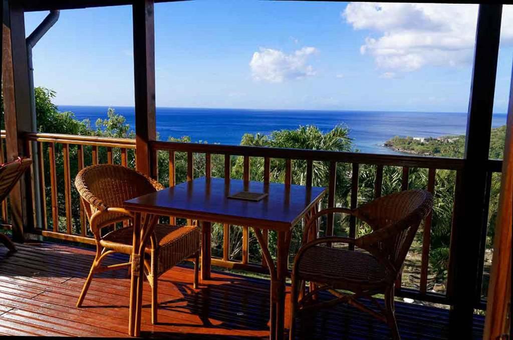 een tafel en stoelen op een balkon met uitzicht op de oceaan bij karureve in Deshaies