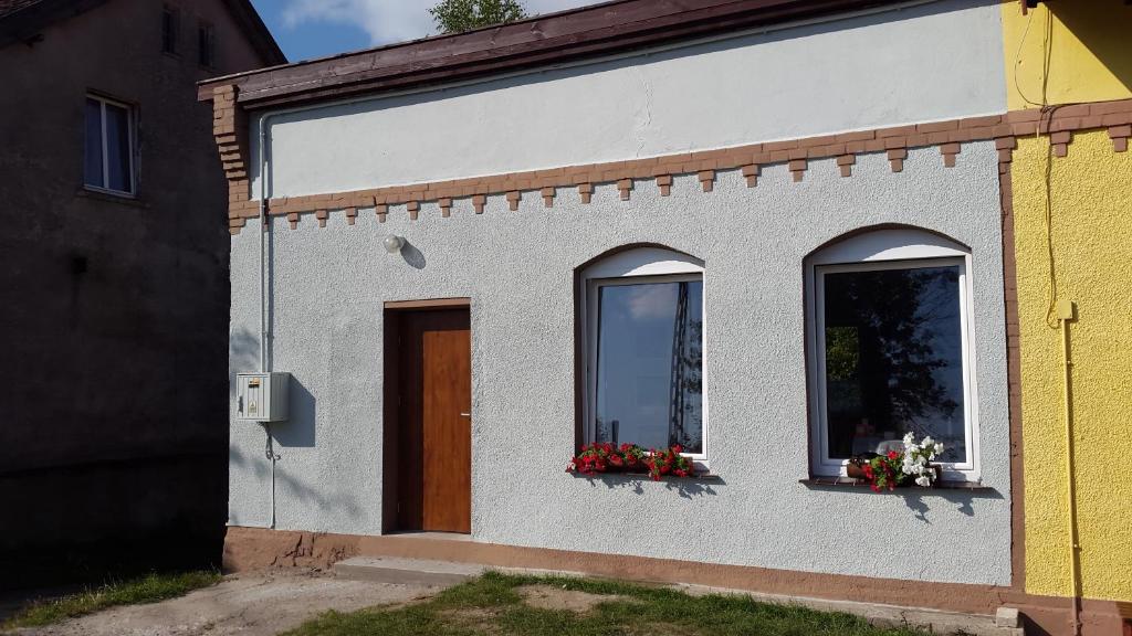 ein weißes Gebäude mit zwei Fenstern und Blumen darauf in der Unterkunft Mazury apartament in Woźnice