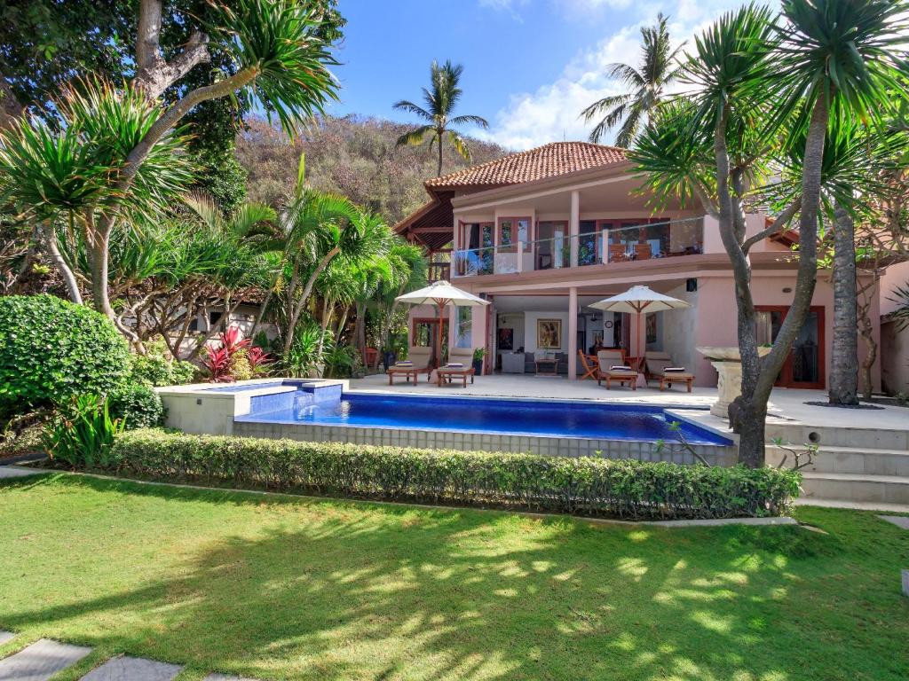 a house with a swimming pool and palm trees at Villa Pantai Candidasa in Candidasa