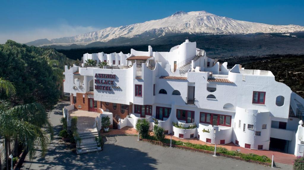 een groot wit gebouw met een berg op de achtergrond bij Assinos Palace Hotel in Giardini Naxos