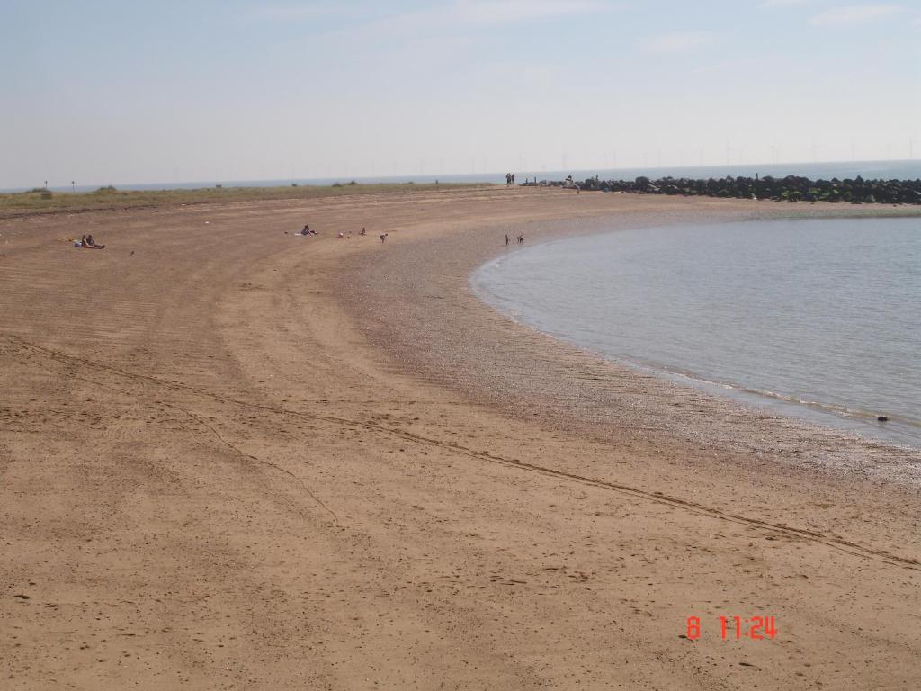 a beach with people sitting on the sand and water at Seaside Cottage in Clacton-on-Sea