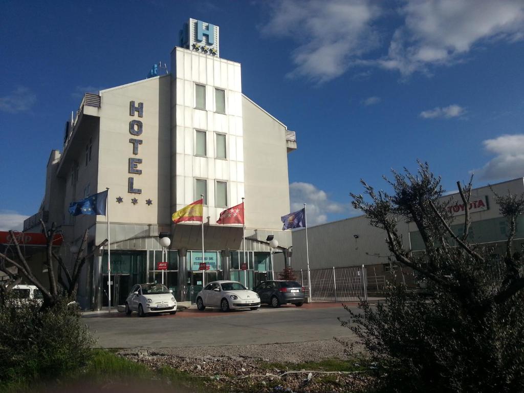 ein Gebäude mit zwei Autos auf einem Parkplatz in der Unterkunft Hotel Ciudad de Fuenlabrada in Fuenlabrada