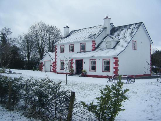 uma casa branca com neve no chão em Heeneys Lodge B&B em Donegal