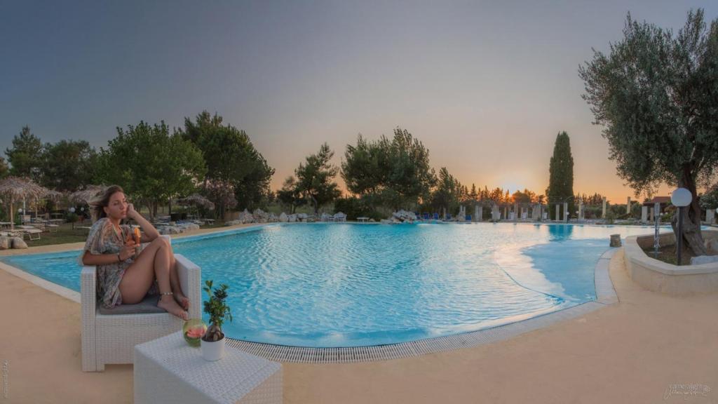 a woman sitting in a chair next to a swimming pool at Villa Conca Marco in Torre dell'Orso