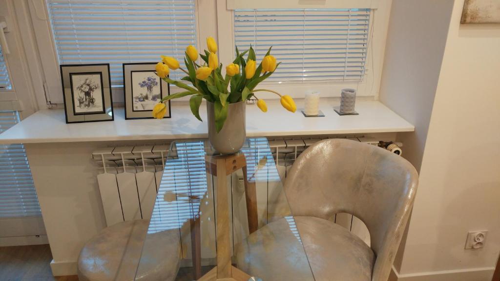 um vaso de flores amarelas sobre uma mesa com uma cadeira em Apartament Centrum em Augustów