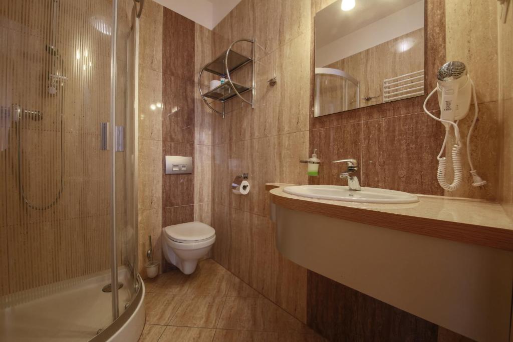 Compact bathroom with corner glass shower, wall-mounted toilet, sink, hairdryer, warm tiled walls.