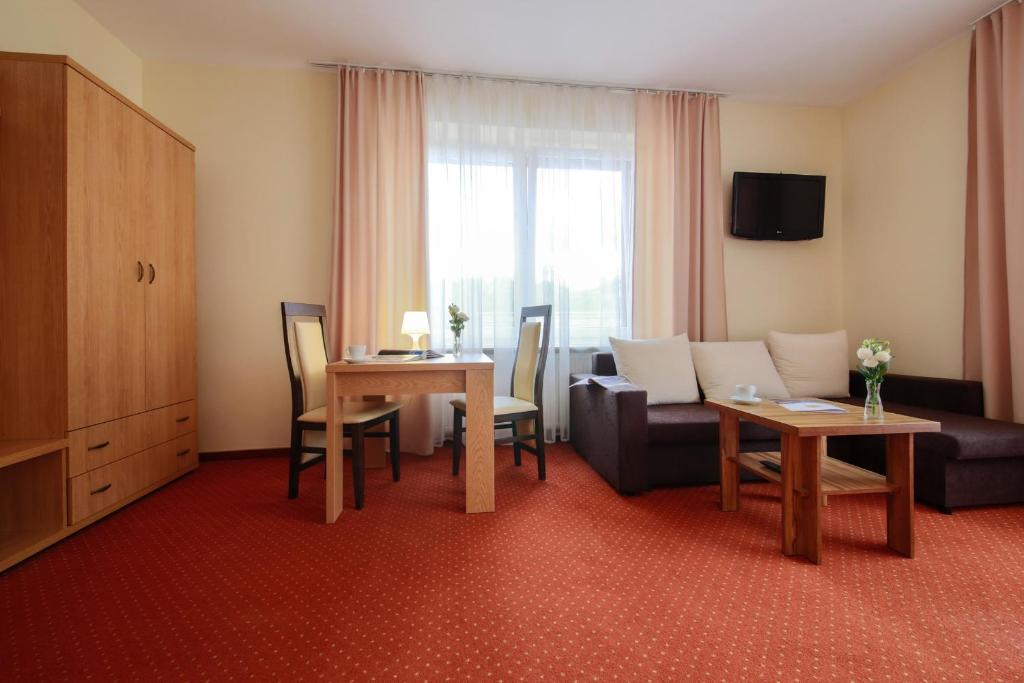 Bright sitting area with dining table, wardrobe, sofa and window draped with sheer curtains.
