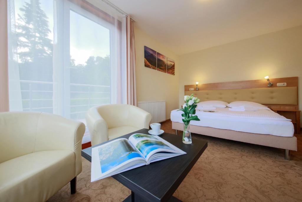 Cozy hotel room seating area with open book on table, vase of flowers, bed near balcony.