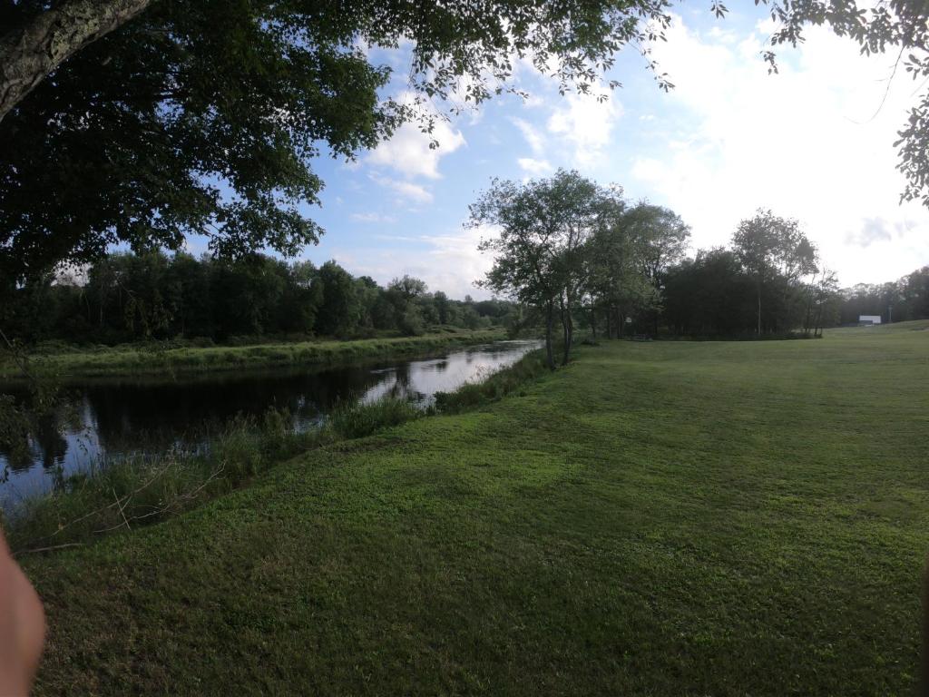 a river next to a field with a grassy field at Copper Lantern Motor Lodge in West Brookfield