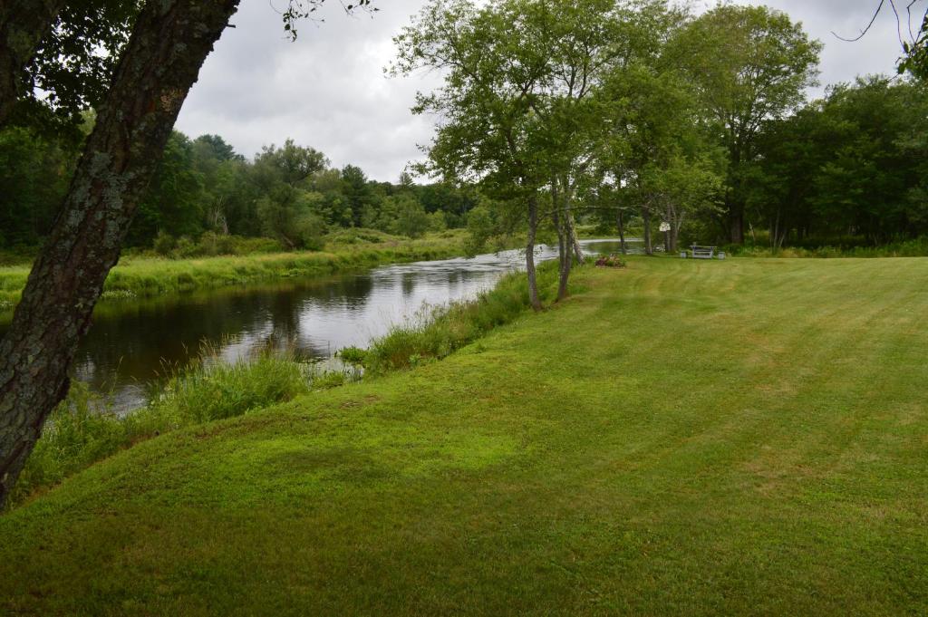 a river with a grassy field next to a river with trees at Copper Lantern Motor Lodge in West Brookfield