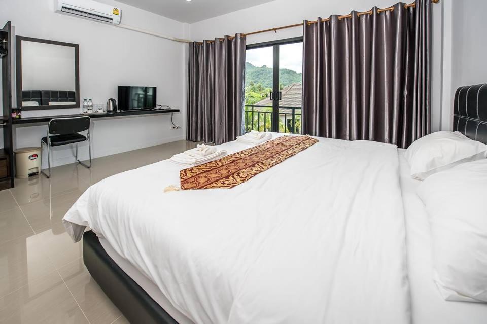 a bedroom with a white bed and a desk and a window at Mr.T Kamala Room in Kamala Beach