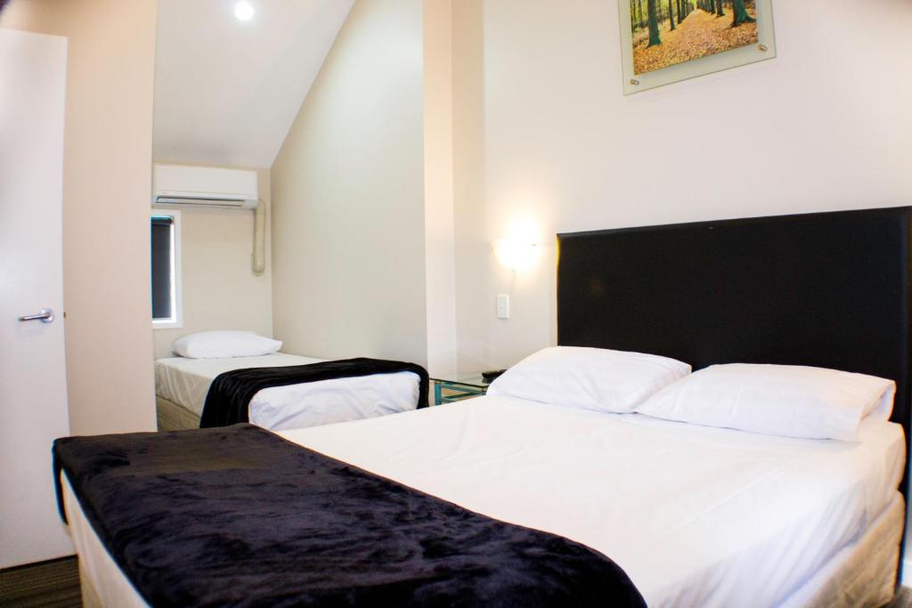 una camera d'albergo con due letti con lenzuola bianche di Rayland Motel ad Auckland