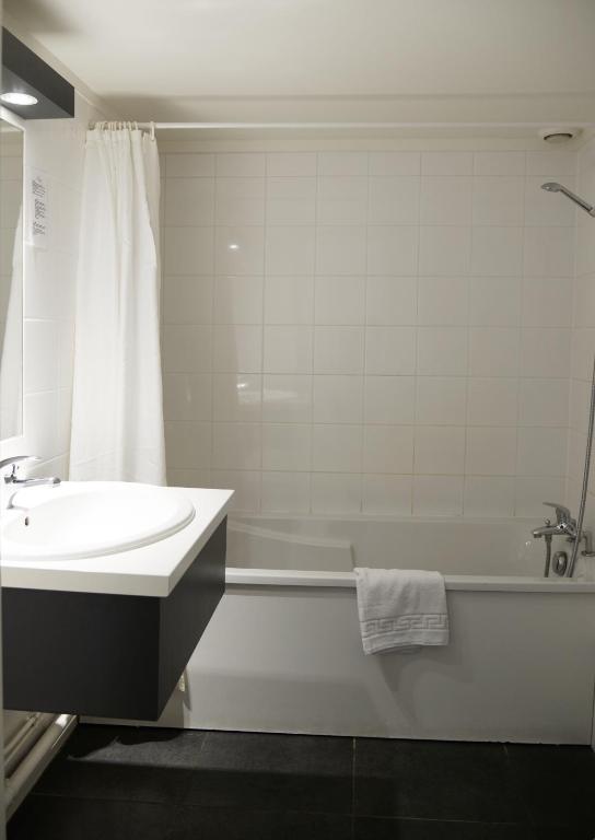 a white bathroom with a sink and a tub and a bath tub at Aerel Hotel Aéroport Blagnac in Blagnac