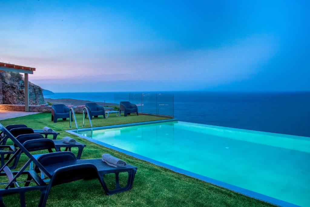 uma piscina com cadeiras e o oceano ao fundo em Anastasis Luxury Villa Andros With Heated Pool em Sinétion