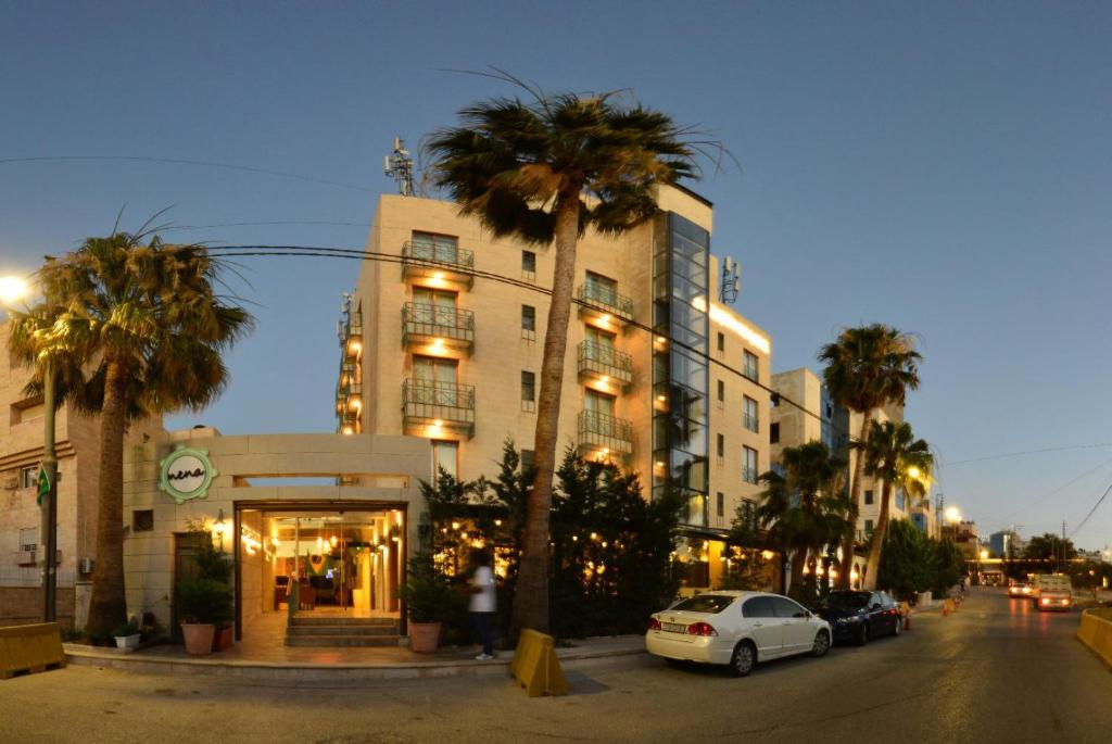 a building with palm trees in front of a street at Guest House Hotel Amman by FHM in Amman