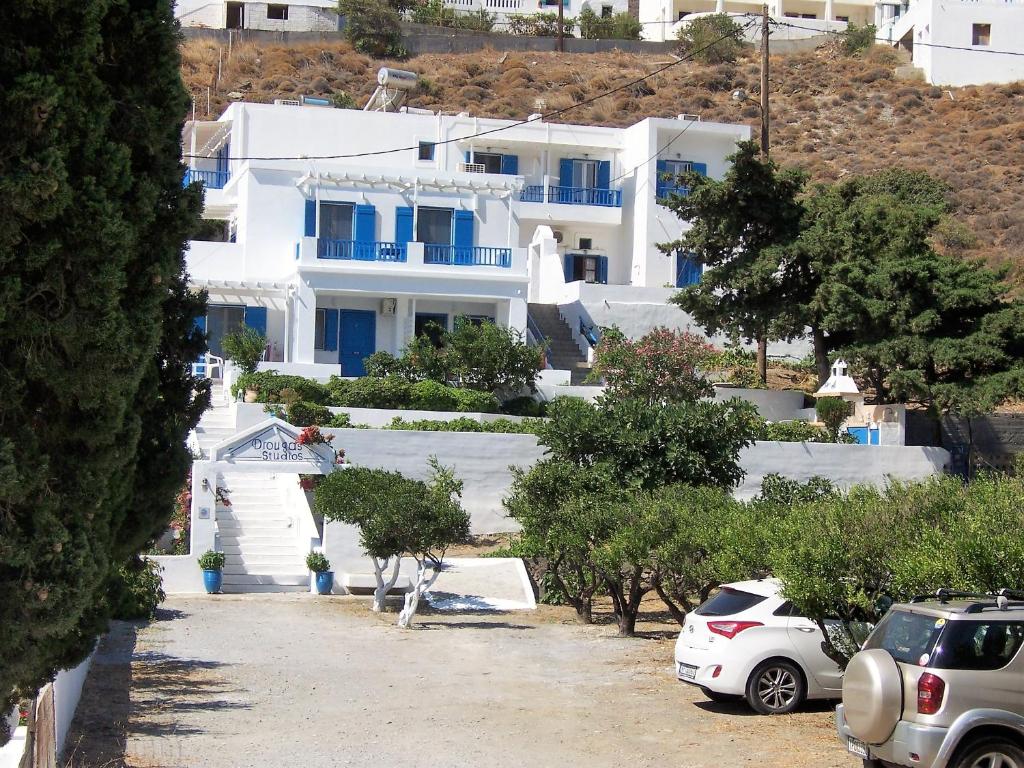 Drouga's Studios & Suites Astypalaia Greece في ليفاذيا أستيبالياس: مبنى ابيض كبير فيه سيارات تقف امامه