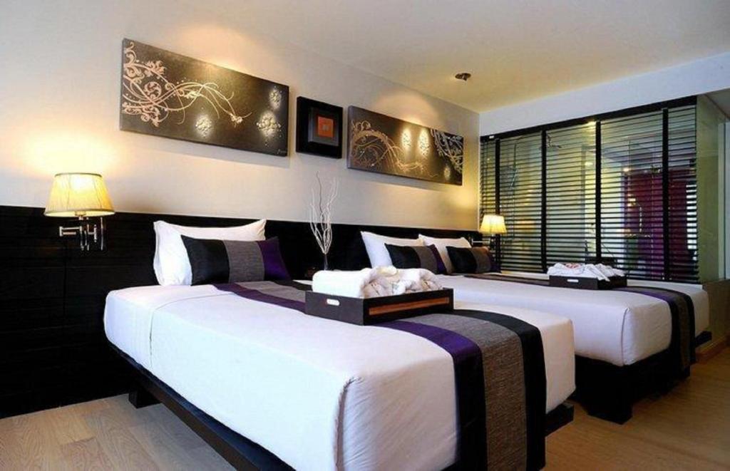 A twin room with two beds, purple accents, and a wide louvered window.