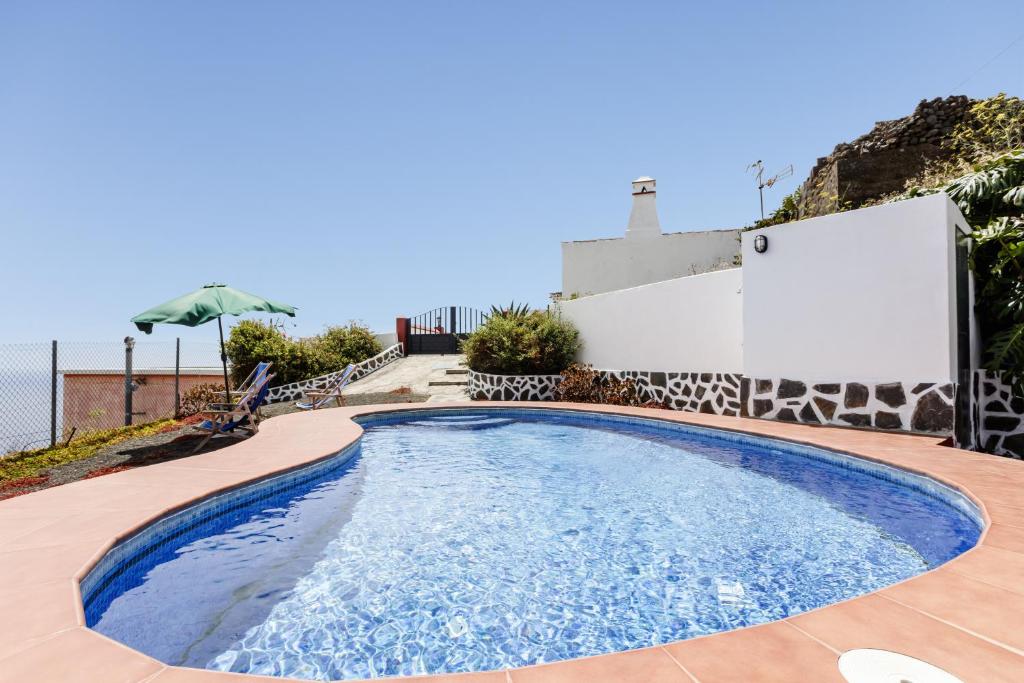 a swimming pool in a backyard with a fence and an umbrella at Tomasín in Puntallana