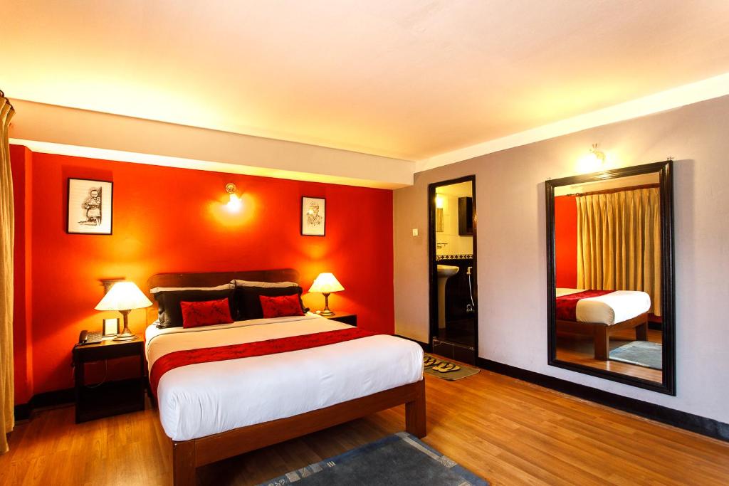 1 dormitorio con paredes de color naranja, 1 cama y espejo en Ambassador Garden Home, en Katmandú