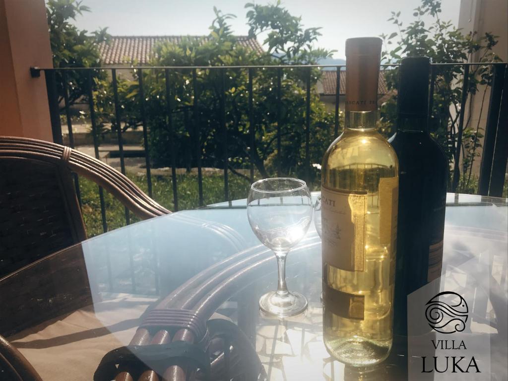 a glass table with a bottle of wine and a wine glass at Apartments Villa Luka in Sveti Stefan
