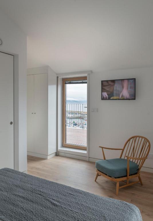 Un dormitorio con una cama y una silla y una ventana. en Hotel SempreFisterra, en Finisterre
