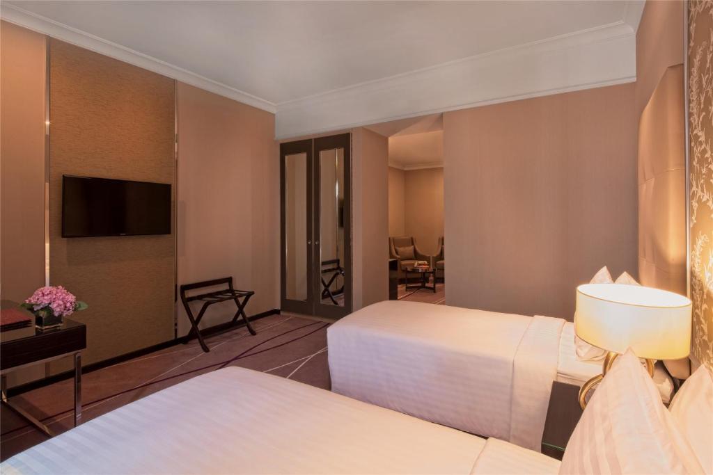 A twin room shows two beds, a wall-mounted television, and a small seating area.