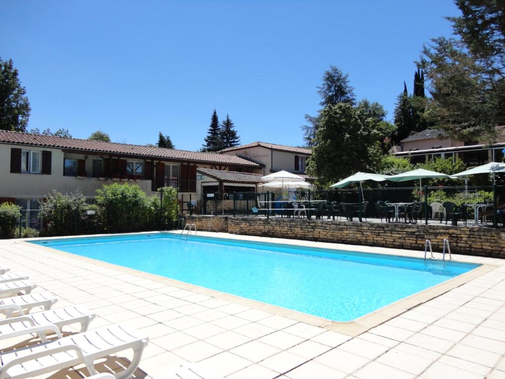 une piscine avec des chaises blanches et un bâtiment dans l'établissement Hôtel Restaurant Les Falaises, à Bouziès