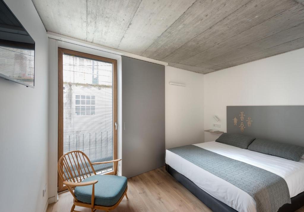 Un dormitorio con una cama y una silla y una ventana. en Hotel SempreFisterra, en Finisterre