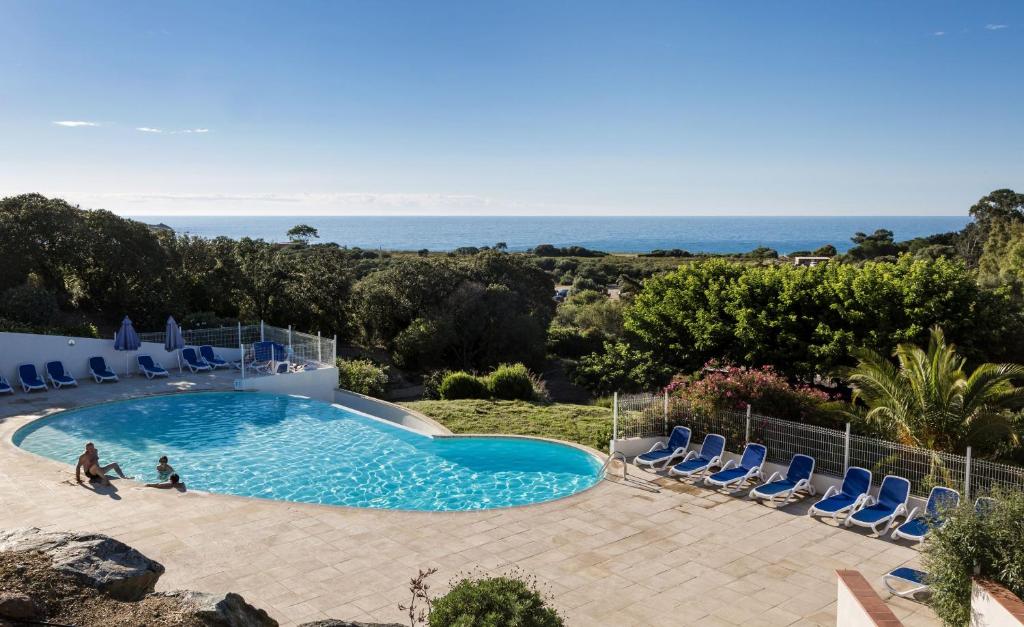 una piscina con sedie e l'oceano sullo sfondo di Résidence Odalys Les Hameaux de Capra Scorsa a Belgodère