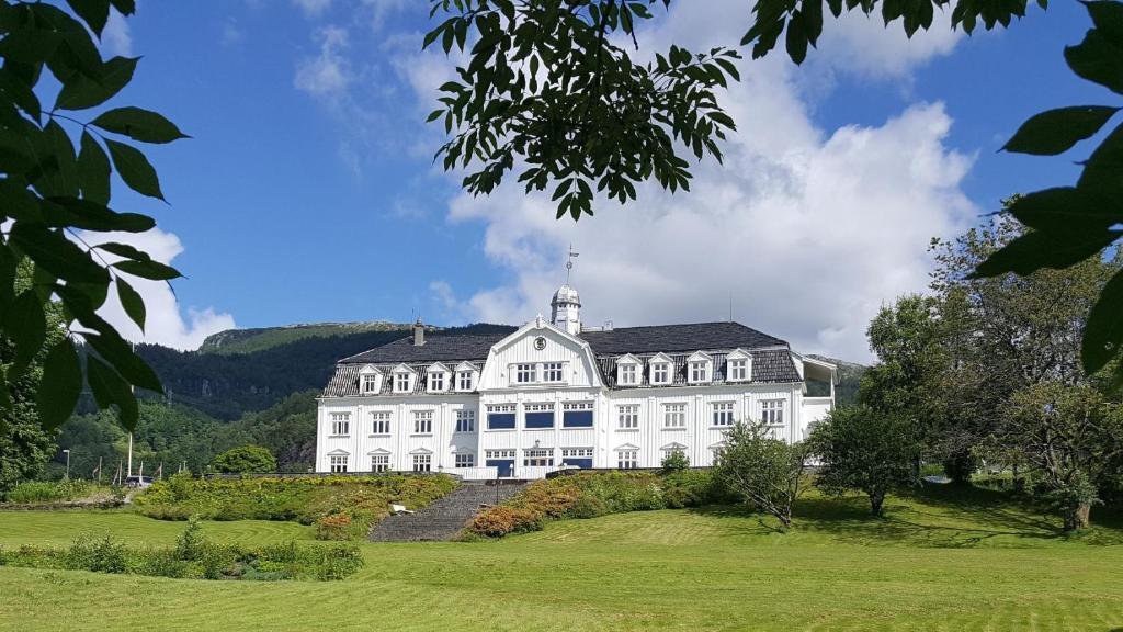 uma grande casa branca no topo de um campo verde em Sauda Fjordhotell em Saudasjøen