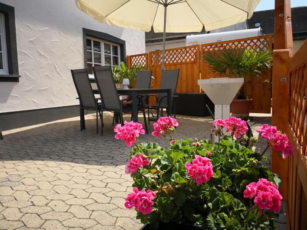 een patio met een tafel en stoelen en roze bloemen bij Maifeld-Fewo Sonnenschein in Kerben