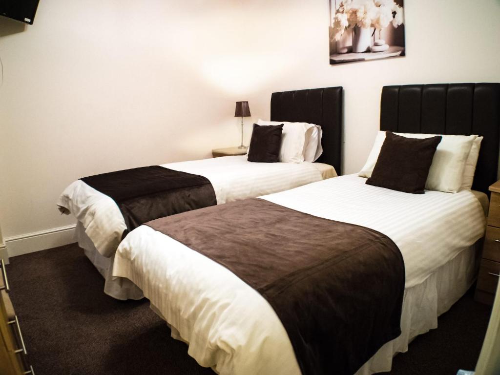 two beds in a hotel room with white and brown sheets at Mereside in Douglas