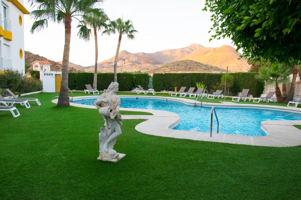 a statue in the grass next to a swimming pool at Hotel Agades in San José