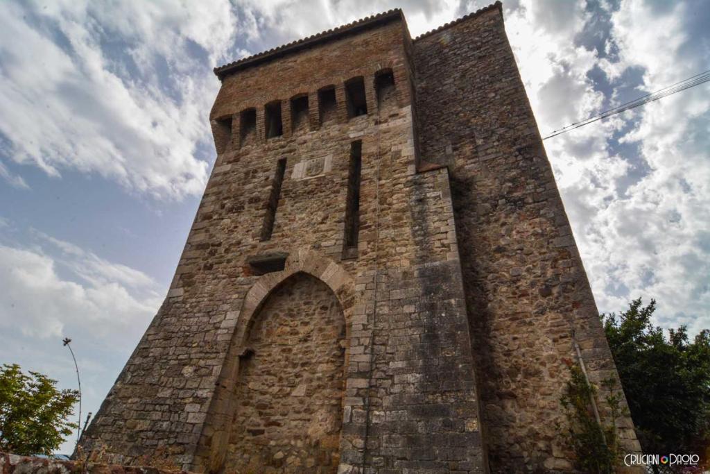 una torre di mattoni alta con un arco su un cielo nuvoloso di Torre Caetani- Night in a medieval tower a Todi