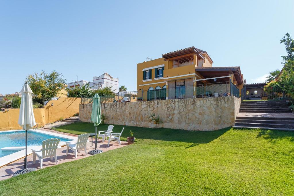 une maison avec une piscine et une cour avec des chaises et des parasols dans l'établissement Bonito Chalet Con Vistas, à Sanlúcar de Barrameda