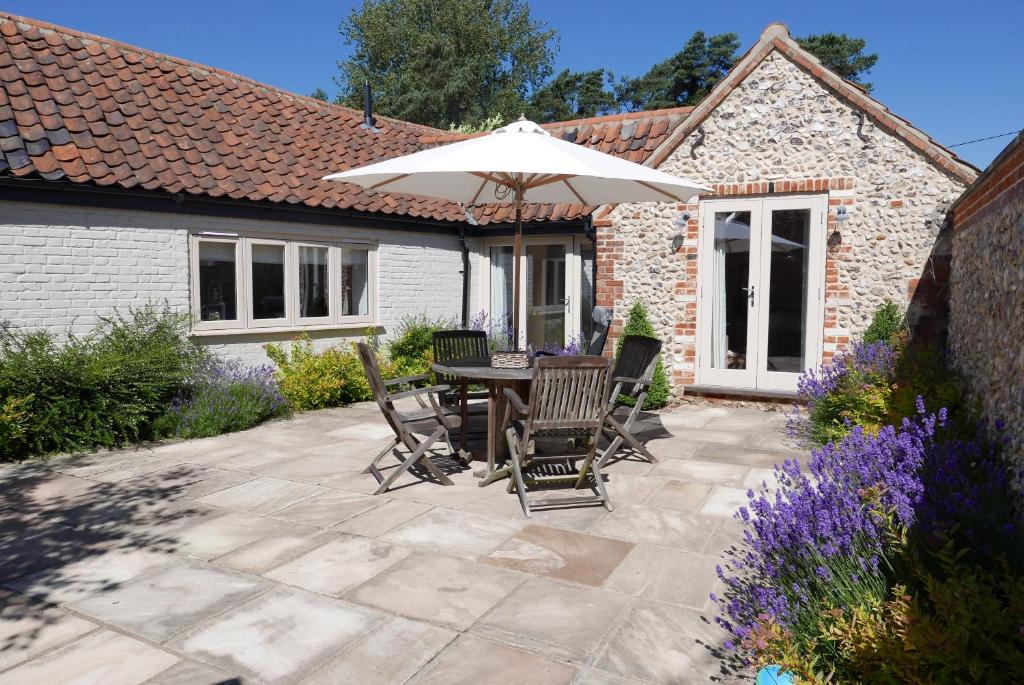 eine Terrasse mit einem Tisch, Stühlen und einem Sonnenschirm in der Unterkunft Bakers Court in East Rudham