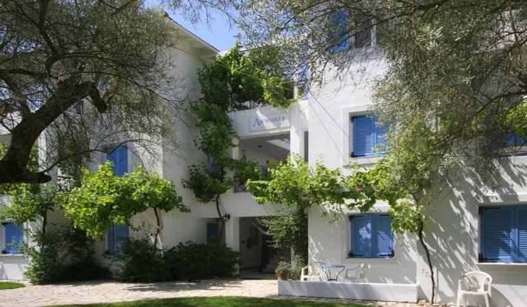 Armonia Apartments في فاسيليكي: مبنى أبيض بنوافذ وأشجار مغلقة زرقاء