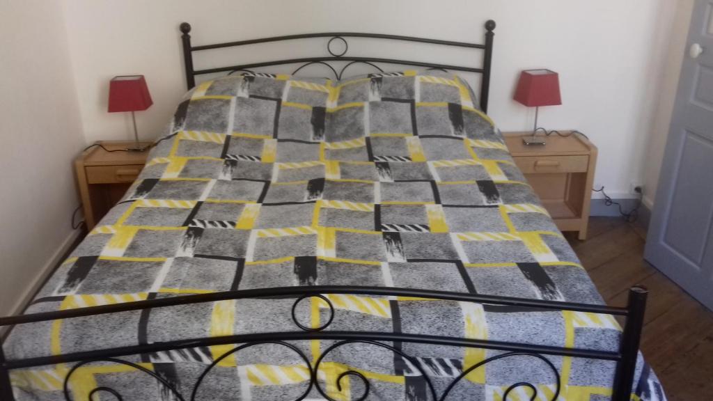 a bed with a yellow and gray comforter and two lamps at La Hall in Thiers